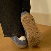 Women's Clipper Sneaker in Cornflower Blue suede, outsole view worn with dark jeans on a wood floor