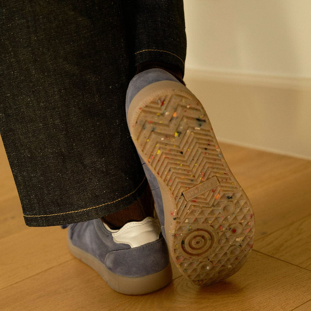 Women's Clipper Sneaker in Cornflower Blue suede, outsole view worn with dark jeans on a wood floor