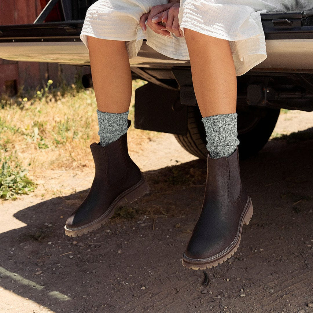 Women's Salt Creek Boot in Dark Chocolate leather, worn with speckled gray socks, seated on a tailgate