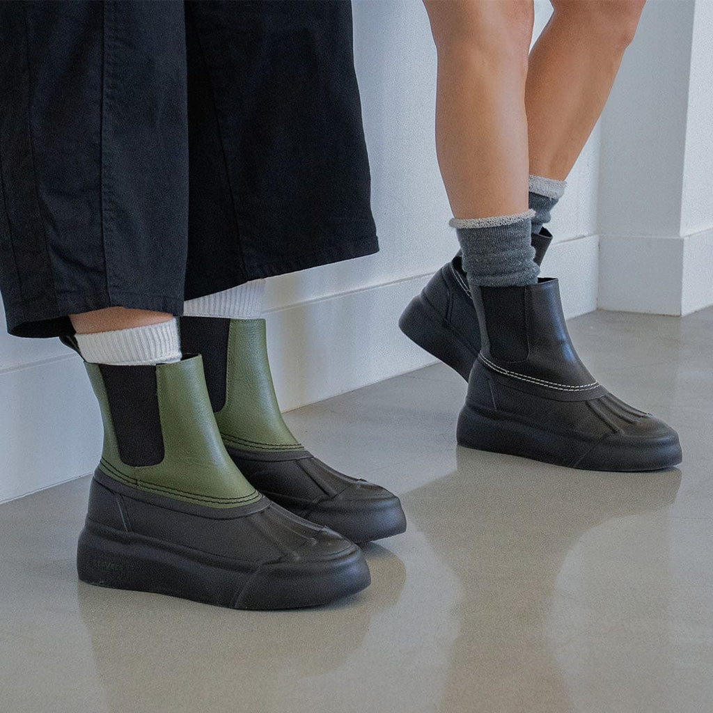Women's Chalet Chelsea Boot in Black leather, worn with black pants and gray socks, beside an olive pair