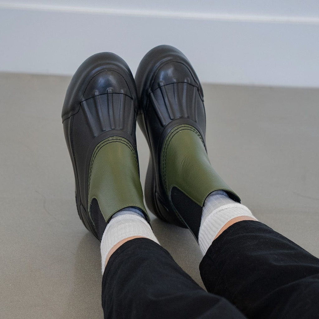 Women's Chalet Chelsea Boot in Utility Olive leather, worn with white socks, feet raised, seated
