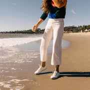 Women's Monterey Sneaker in Bleach canvas, worn with white cropped pants, walking on the shoreline