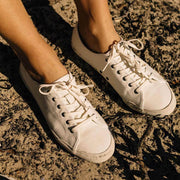 Women's Monterey Sneaker in Bleach canvas, worn bare-ankled on rough sandy ground, close up