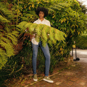 Women's Baja Slip On in Surplus Green canvas, worn with jeans, full-length view among ferns