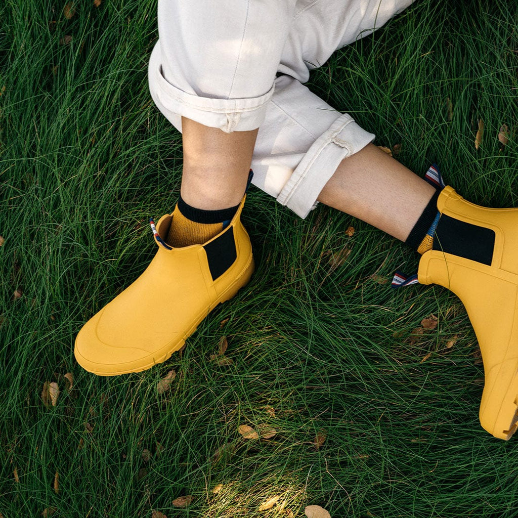 Women's Bolinas Off Shore Boot in Calendula rubber, close-up worn with cuffed white pants on grass