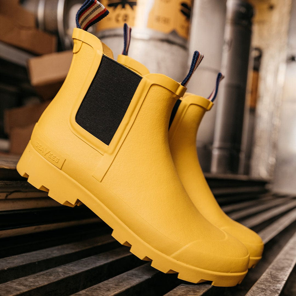 Women's Bolinas Off Shore Boot in Calendula rubber, close-up of the pair on a wooden floor, elastic side panel visible