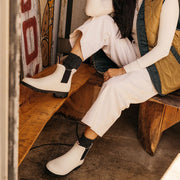Women's Bolinas Off Shore Boot in Salt rubber, worn with white pants, feet resting on wooden furniture