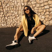 Women's Bolinas Off Shore Boot in Salt rubber, worn by a person seated on pavement in a yellow cardigan