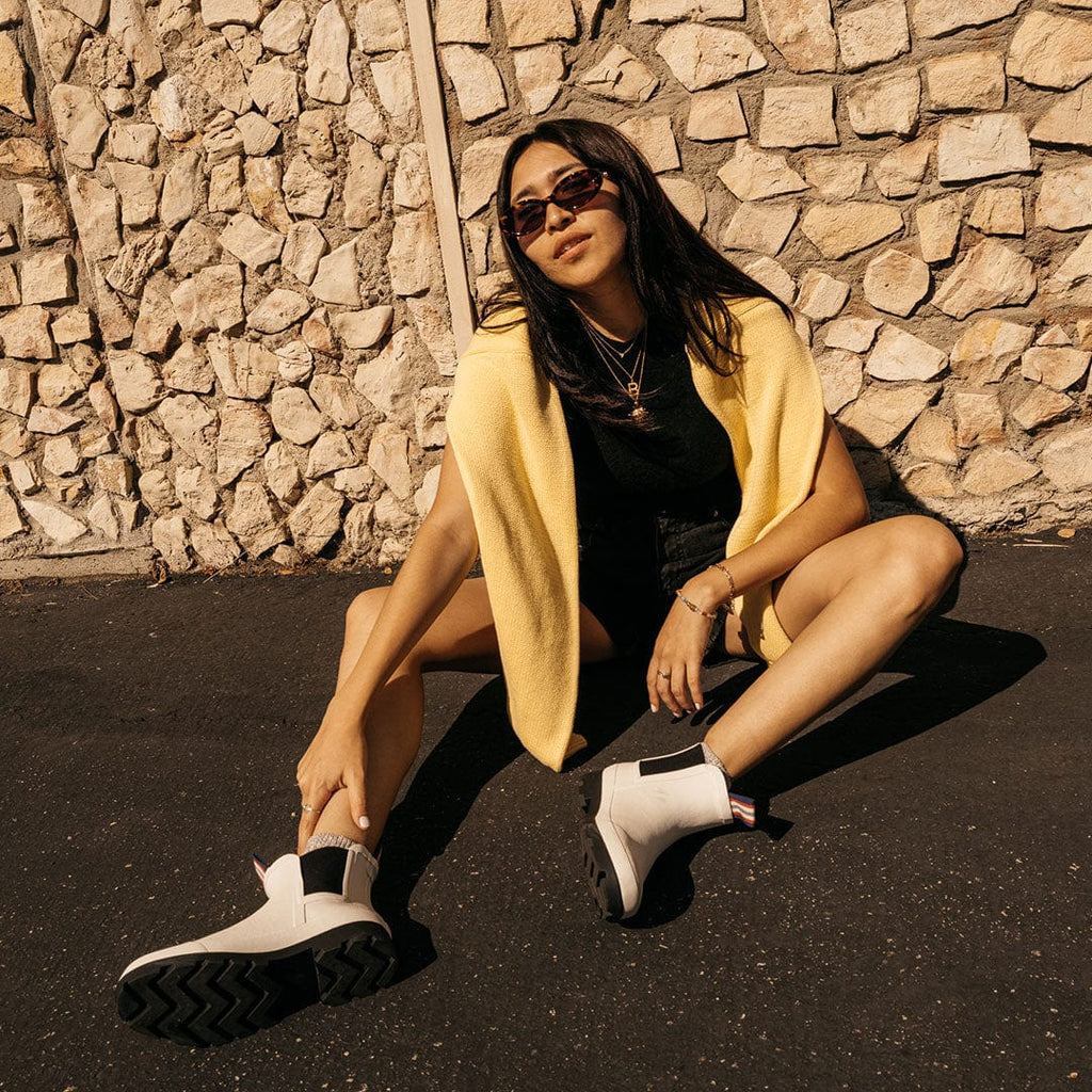 Women's Bolinas Off Shore Boot in Salt rubber, worn by a person seated on pavement in a yellow cardigan